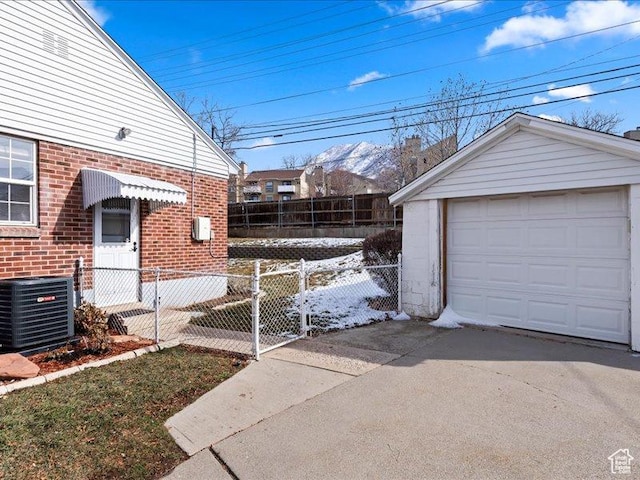 view of side of property with cooling unit, brick siding, driveway, fence, and a garage