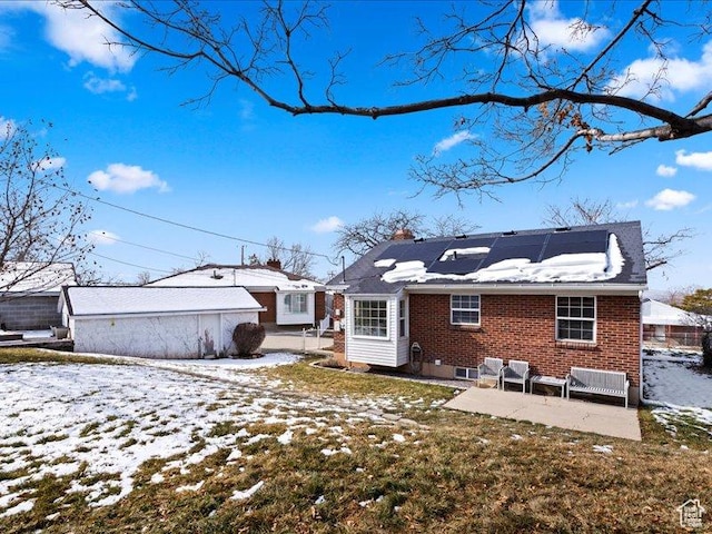 snow covered house featuring solar panels, brick siding, and a patio