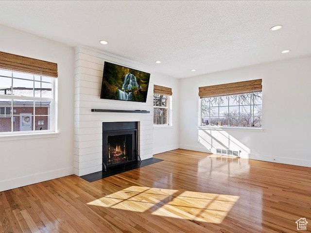 unfurnished living room featuring healthy amount of natural light, a fireplace, wood finished floors, recessed lighting, and a textured ceiling