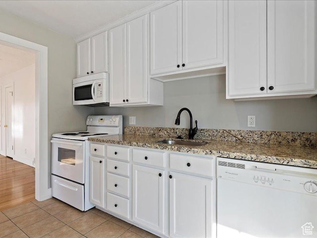 kitchen with white appliances, a sink, white cabinets, light stone counters, and light tile patterned floors