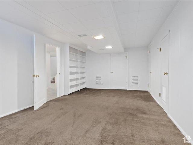 empty room featuring carpet, built in shelves, and baseboards