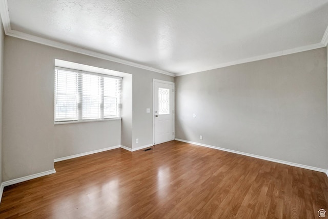 empty room featuring crown molding, wood finished floors, and baseboards