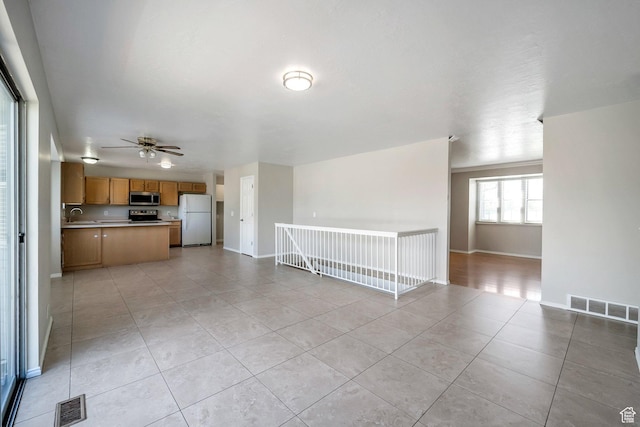 unfurnished living room featuring light tile patterned floors, ceiling fan, baseboards, and a sink