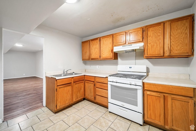 kitchen featuring white gas range, under cabinet range hood, a sink, light countertops, and brown cabinetry