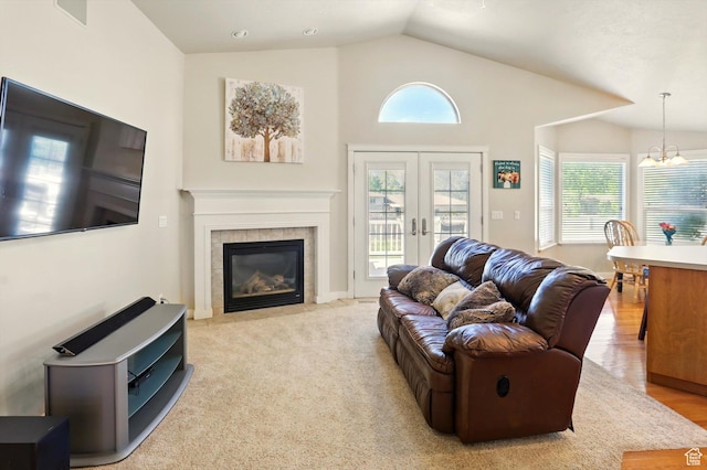 living room with vaulted ceiling, a chandelier, a tile fireplace, and french doors