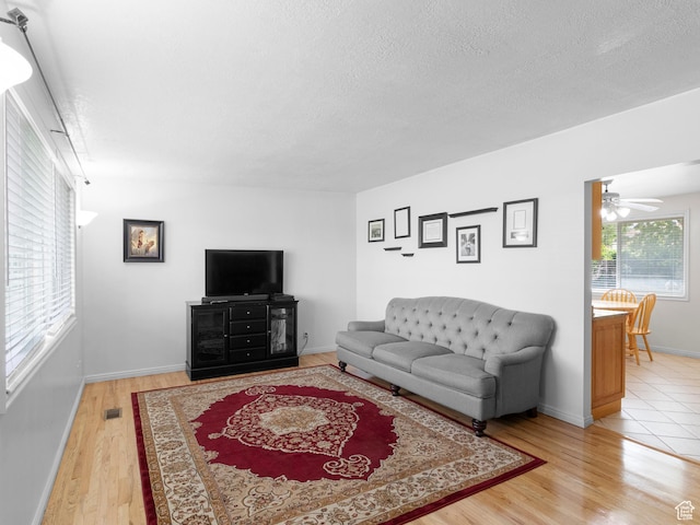living room with light wood finished floors, a textured ceiling, ceiling fan, and baseboards