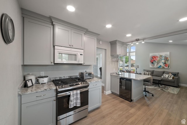 kitchen featuring gas range, white microwave, gray cabinets, open floor plan, and light wood-type flooring