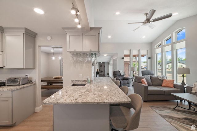 kitchen featuring a sink, a kitchen breakfast bar, a ceiling fan, a peninsula, and light wood finished floors