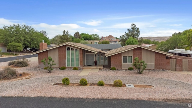 mid-century modern home with a chimney, solar panels, and brick siding