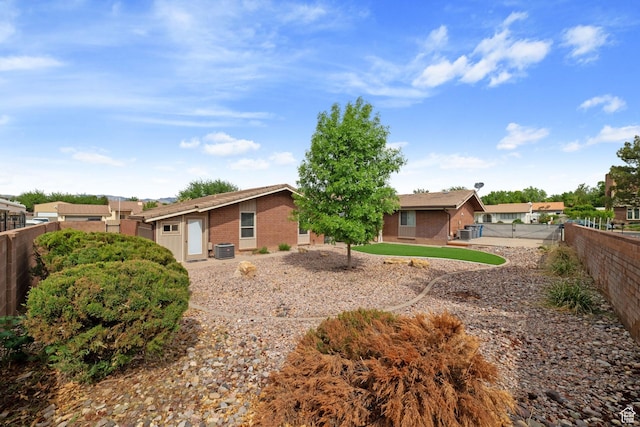 view of front of house featuring brick siding, a fenced backyard, and central AC