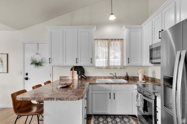kitchen featuring stainless steel appliances, a sink, vaulted ceiling, a breakfast bar, and white cabinets