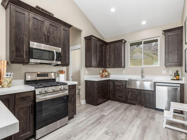 kitchen with appliances with stainless steel finishes, a sink, lofted ceiling, dark brown cabinets, and light countertops