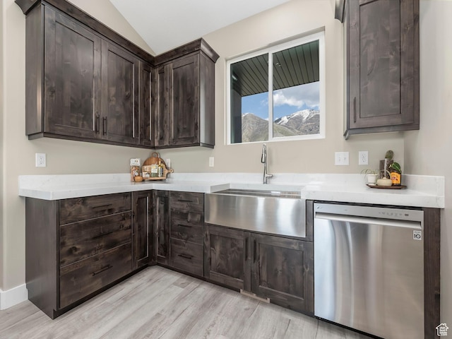 kitchen featuring stainless steel dishwasher, a sink, dark brown cabinets, light wood-type flooring, and lofted ceiling