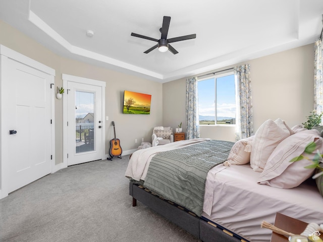 bedroom featuring access to outside, a tray ceiling, multiple windows, and carpet