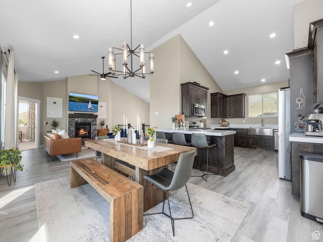 dining room with light wood finished floors, a fireplace, a chandelier, recessed lighting, and high vaulted ceiling