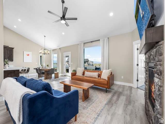 living area featuring a chandelier, a ceiling fan, light wood finished floors, a stone fireplace, and baseboards