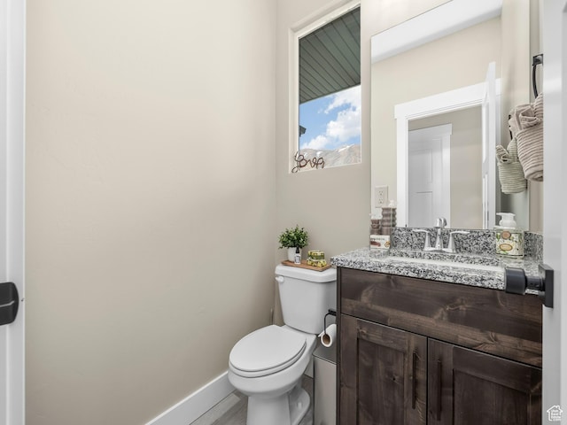 half bath featuring toilet, vanity, and baseboards