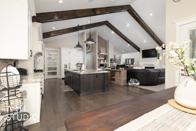kitchen with a fireplace, a sink, white cabinetry, a kitchen island with sink, and beamed ceiling