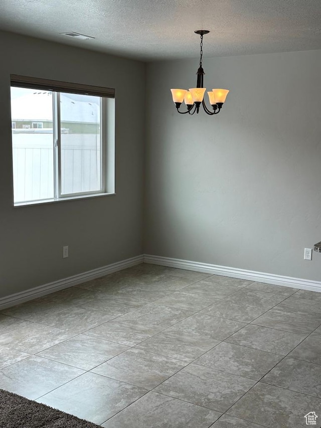 empty room with a chandelier, a textured ceiling, and baseboards