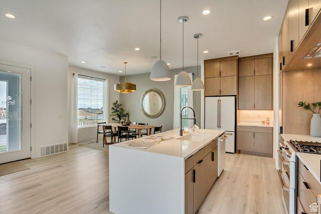 kitchen with white appliances, a sink, light wood-style flooring, light countertops, and decorative light fixtures