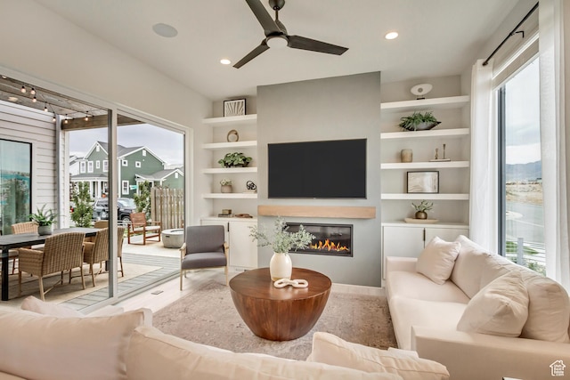 living area featuring healthy amount of natural light, a glass covered fireplace, built in features, ceiling fan, and recessed lighting