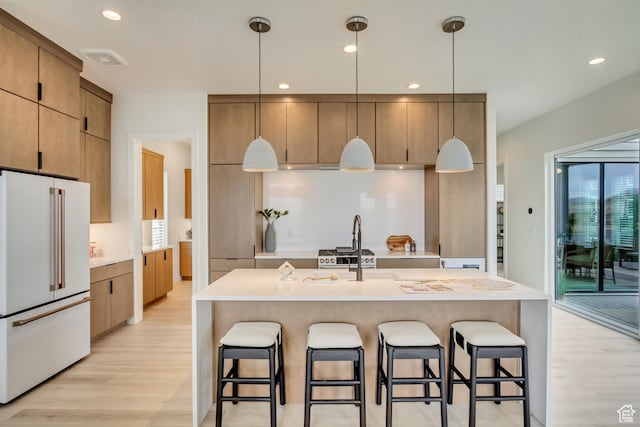 kitchen with high end white refrigerator, light wood-style floors, a breakfast bar, recessed lighting, and light countertops