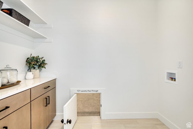 washroom featuring hookup for a washing machine, cabinet space, baseboards, and light tile patterned floors