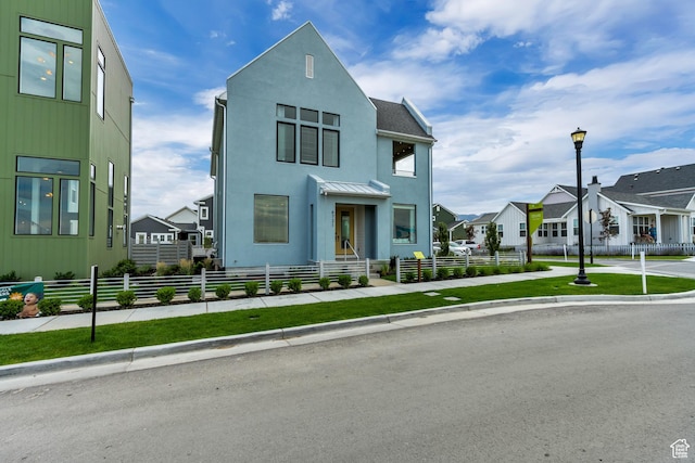 view of front facade featuring a residential view, a fenced front yard, stucco siding, and a standing seam roof