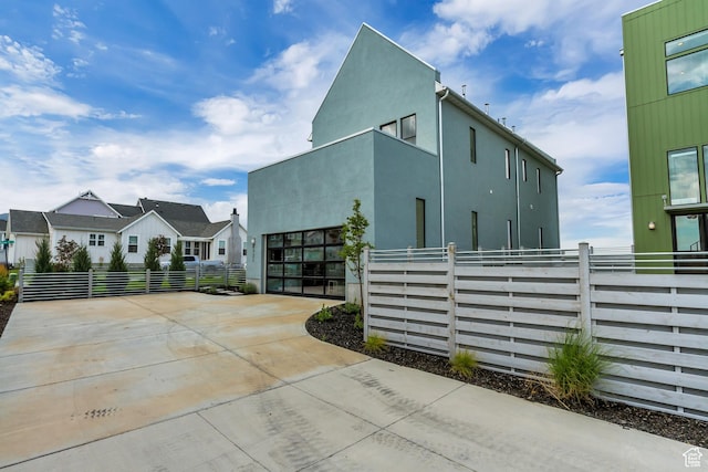 view of side of home featuring concrete driveway, fence, an attached garage, and stucco siding