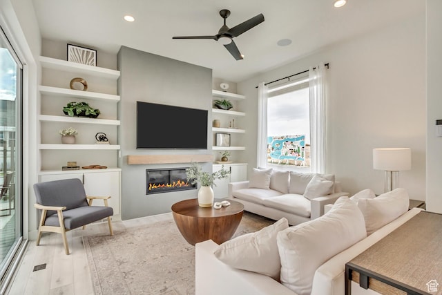 living area with ceiling fan, a glass covered fireplace, recessed lighting, and wood finished floors