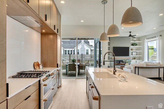 kitchen with double oven range, a sink, a ceiling fan, light wood finished floors, and light countertops