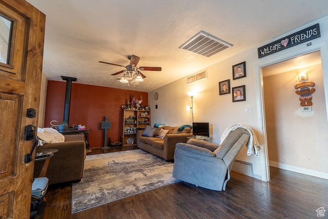 living area featuring a wood stove, a ceiling fan, wood finished floors, and baseboards