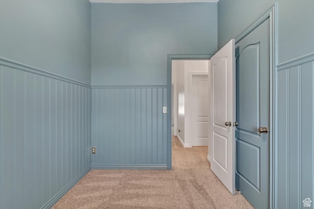 unfurnished room featuring light colored carpet and a wainscoted wall