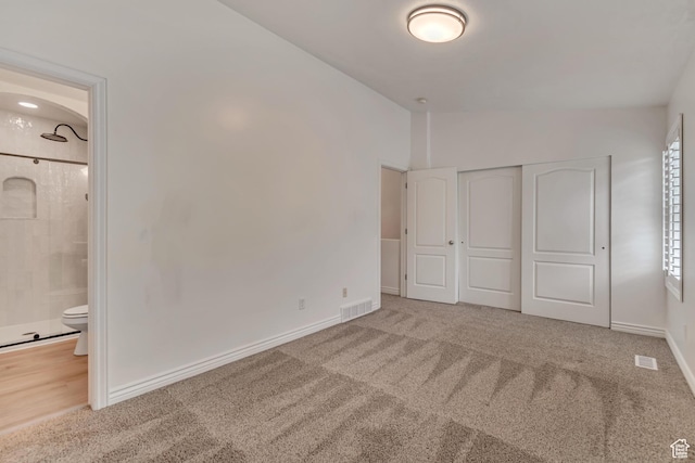 unfurnished bedroom featuring carpet, ensuite bath, vaulted ceiling, and a closet