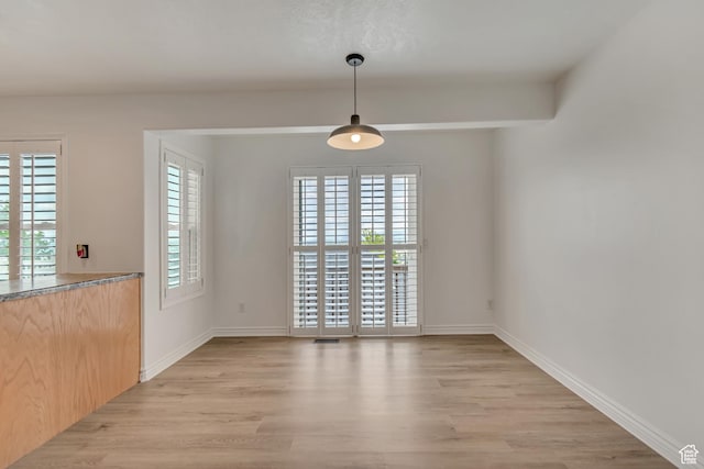 unfurnished dining area featuring light wood-style flooring, plenty of natural light, and baseboards