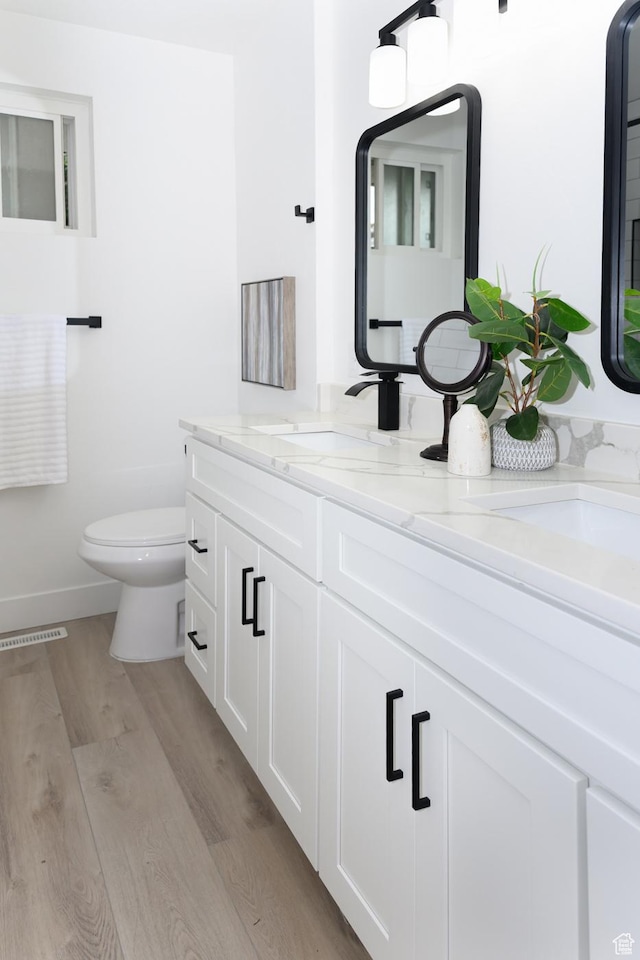 bathroom with wood finished floors, toilet, double vanity, and baseboards