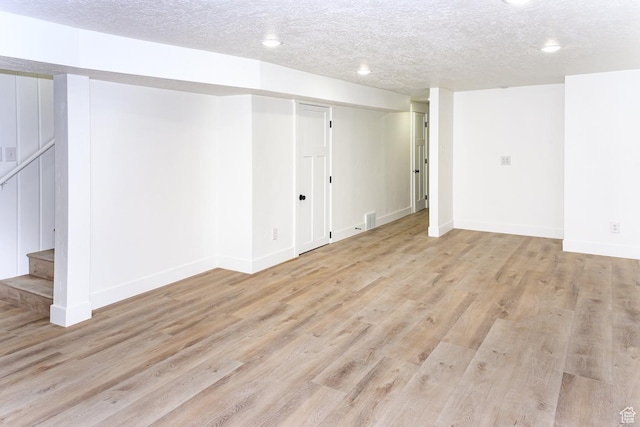 finished basement featuring light wood finished floors, baseboards, recessed lighting, a textured ceiling, and stairway