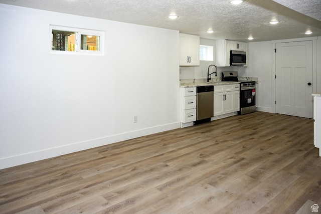 kitchen featuring appliances with stainless steel finishes, white cabinetry, light wood-type flooring, baseboards, and a textured ceiling