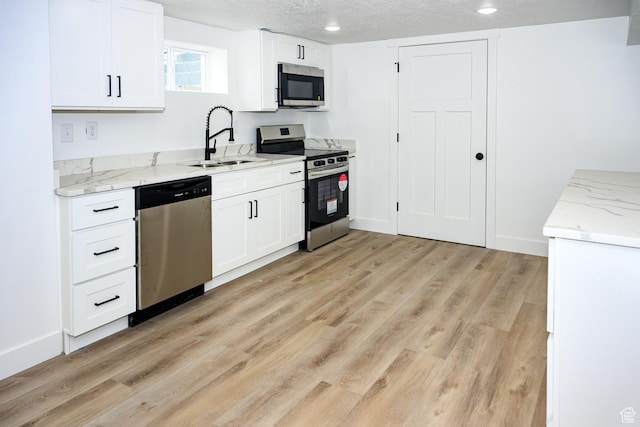 kitchen featuring appliances with stainless steel finishes, a sink, light wood-style floors, white cabinets, and a textured ceiling