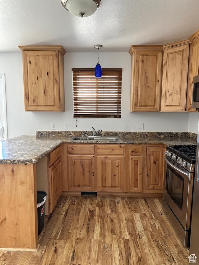 kitchen featuring a sink, appliances with stainless steel finishes, light wood-style flooring, dark stone counters, and pendant lighting