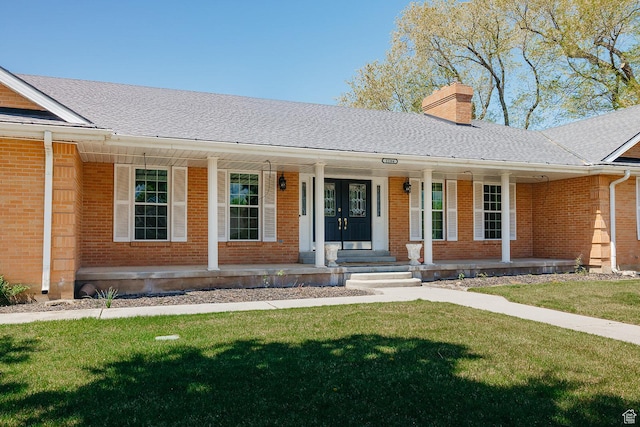 ranch-style home with covered porch, a chimney, brick siding, and a front yard