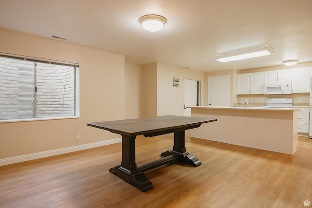 unfurnished dining area featuring light wood-style flooring, a sink, and baseboards