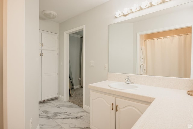 full bathroom with marble finish floors, vanity, and baseboards