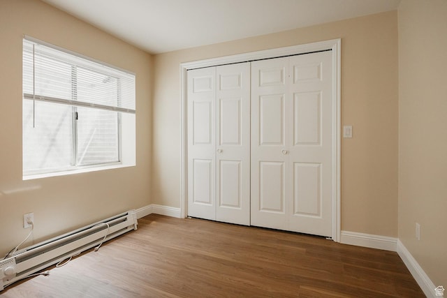 unfurnished bedroom featuring a baseboard heating unit, wood finished floors, a closet, and baseboards