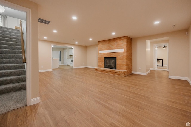 unfurnished living room with stairs, a brick fireplace, light wood-style flooring, baseboards, and recessed lighting
