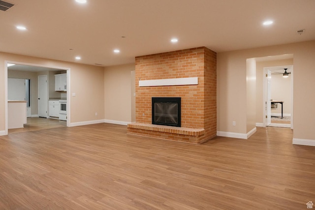 unfurnished living room featuring light wood finished floors, baseboards, a brick fireplace, and recessed lighting