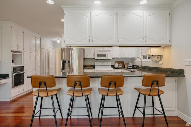 kitchen with white appliances, a peninsula, a sink, white cabinets, and dark countertops