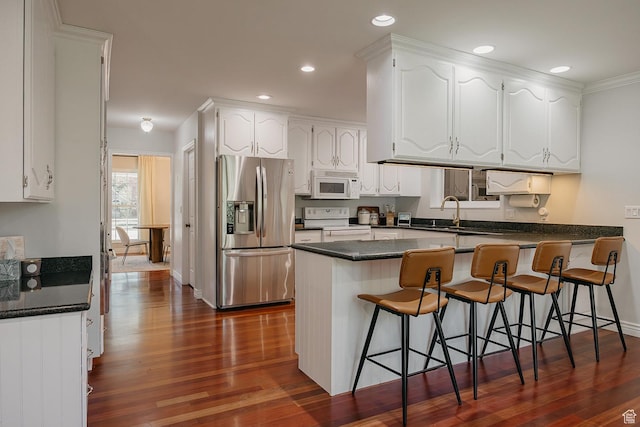 kitchen with white appliances, a peninsula, dark countertops, white cabinetry, and recessed lighting