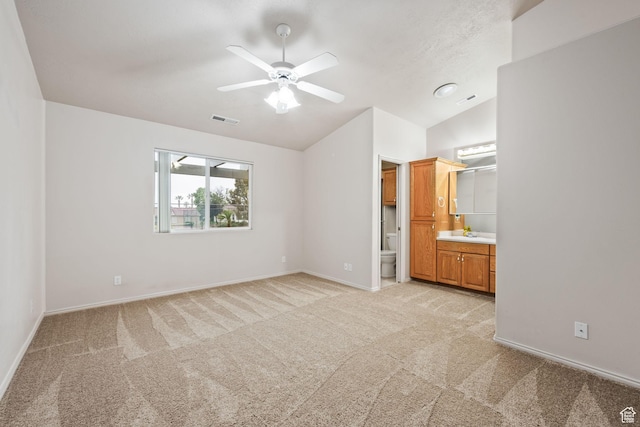 unfurnished bedroom with light carpet, lofted ceiling, baseboards, ensuite bath, and a sink