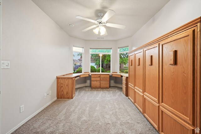 unfurnished office with light colored carpet, a ceiling fan, and baseboards
